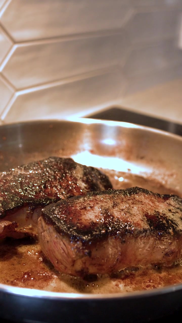 Primo piano di bistecche di manzo condite che sfrigolano nel burro bollente su un fornello da cucina.