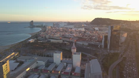 Aerial-panoramic-view-of-sea-coast-and-surrounding-borough-with-port.-Scene-lit-by-setting-sun.-Barcelona,-Spain