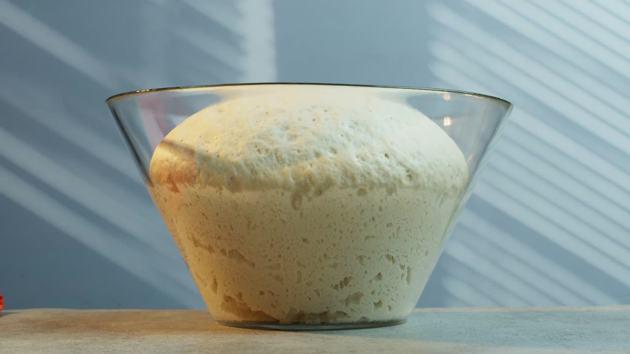 Watch a close-up time-lapse of fresh bread dough rising naturally in a glass bowl, perfect for baking, cooking, or ASMR visuals