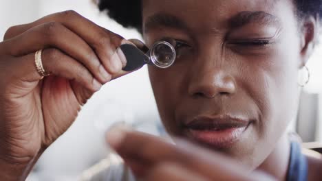 African-american-female-worker-inspecting-ring-with-magnifying-glass-in-workshop-in-slow-motion