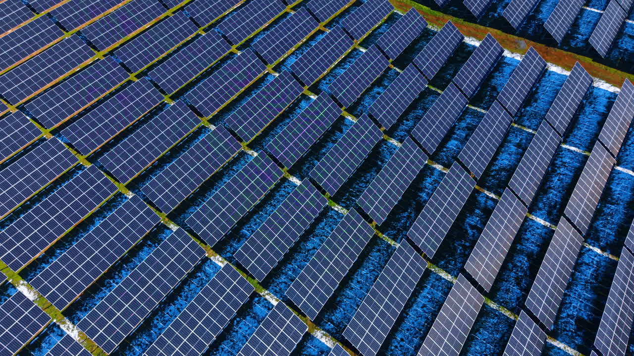 Fila diagonale di pannelli solari su terreno invernale. Vista dall'alto di pannelli fotovoltaici disposti in linee diagonali attraverso un campo con chiazze di neve