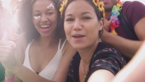 grupo de jóvenes amigos bailando detrás de una barrera tomando selfies en un festival de música al aire libre