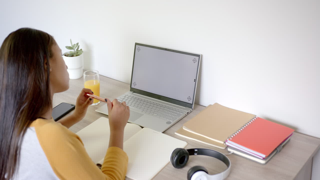 Studying at home, asian woman using laptop and writing in notebook with headphones nearby, copy spac