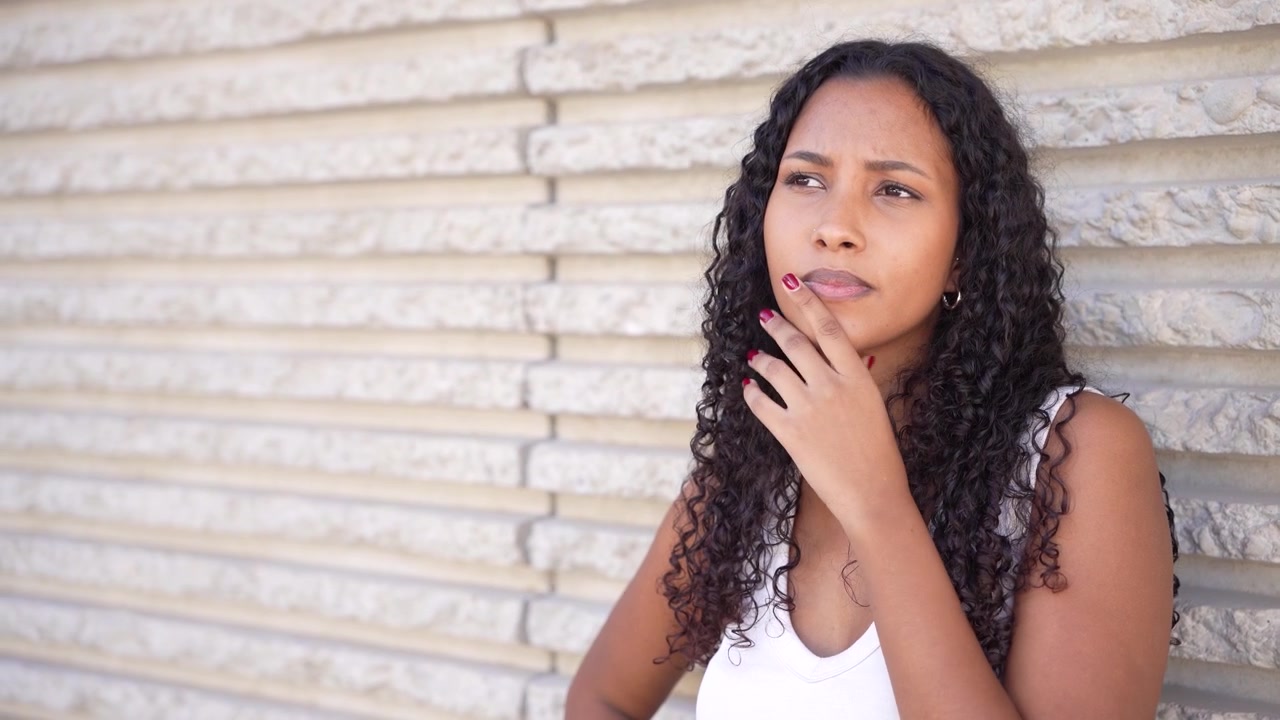Una donna sicura di sé posa contro una parete texturizzata, immersa nella luce naturale.