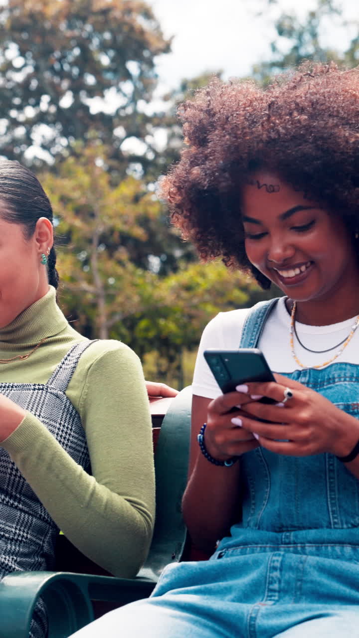 Happy Young Women Friends Using Smartphones on a Park Bench