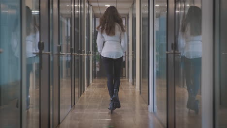 rear view of businesswoman riding along corridor in modern office on scooter