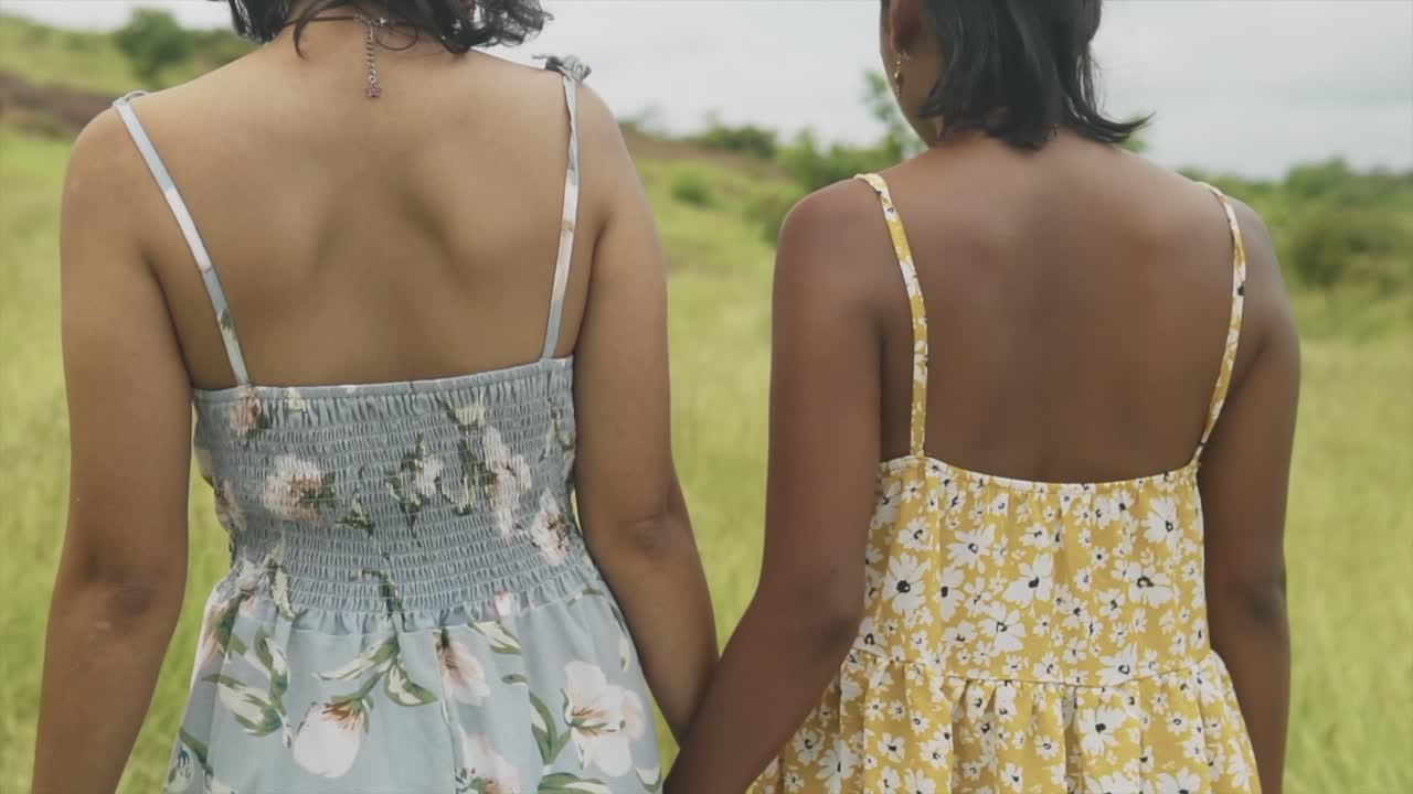 Ripresa intima al rallentatore di due ragazze che si tengono per mano e si allontanano in un campo con erba alta.