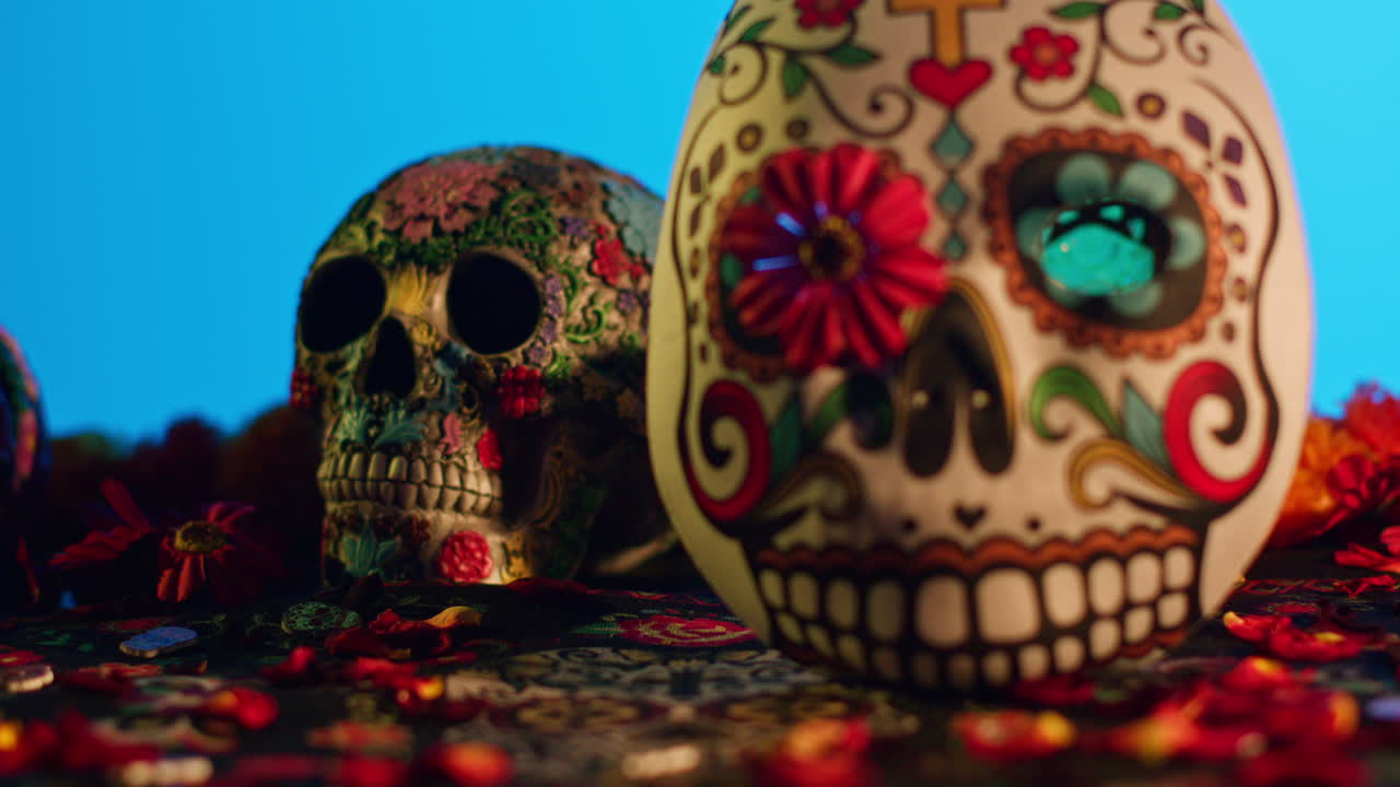 close up de cráneos y máscaras decoradas rodeadas de pétalos de flores celebrando la fiesta mexicana de dia de muertos o día de los muertos contra un fondo azul