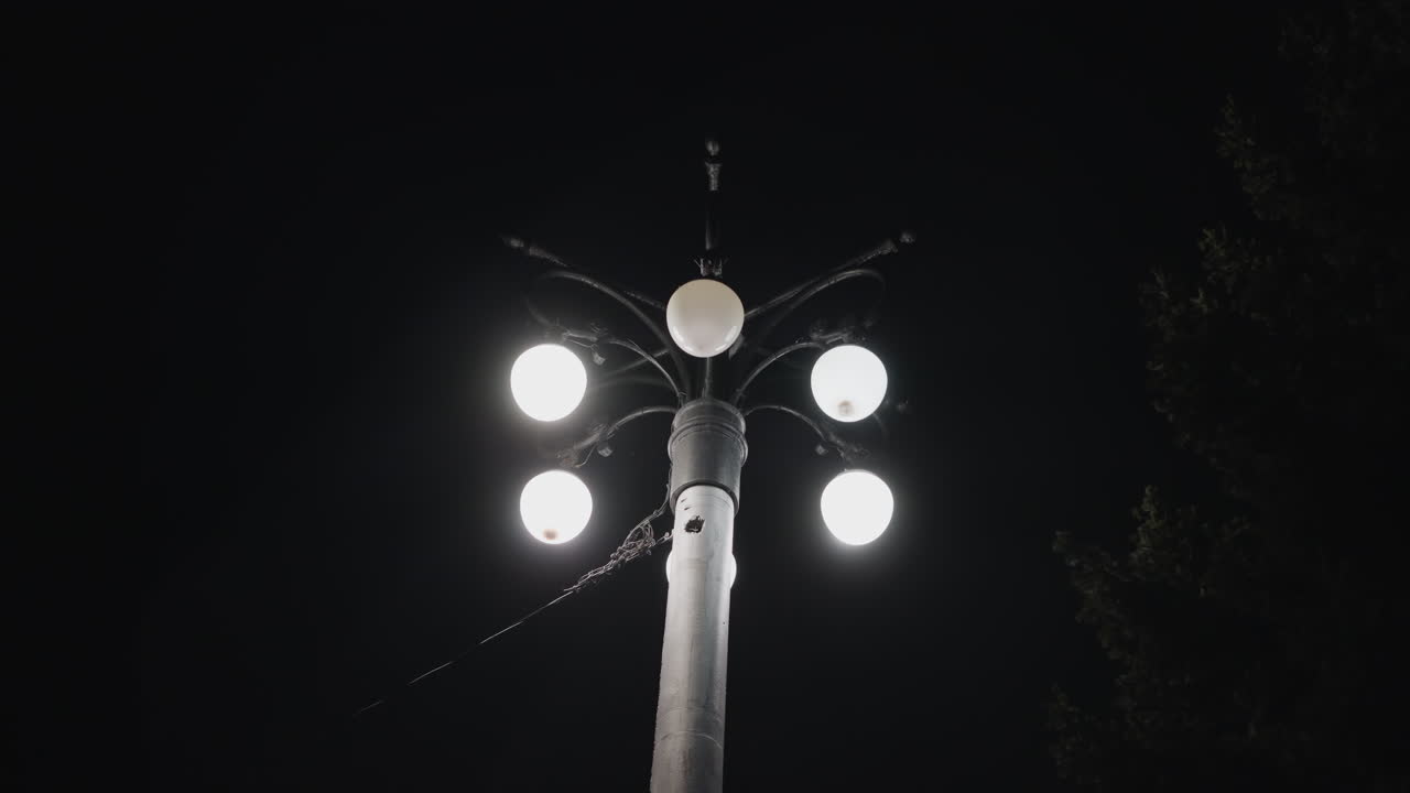 vista de cerca de un poste de farola con cinco bombillas iluminadas contra un cielo oscuro. una de las bombillas está parpadeando