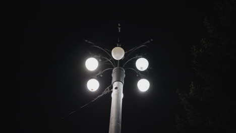 vista de cerca de un poste de farola con cinco bombillas iluminadas contra un cielo oscuro. una de las bombillas está parpadeando