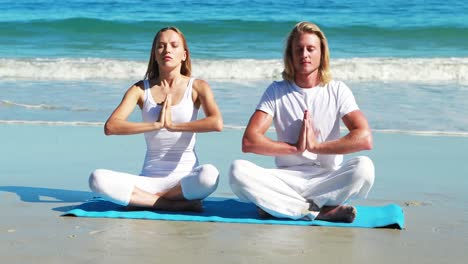 couple performing yoga at beach
