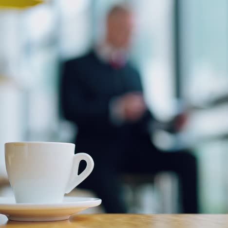 white cup of coffee on the table in the office. coffee cup on the blur background of a businessman working with papers.