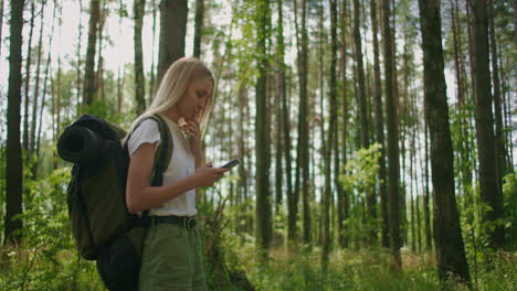 mujer atractiva relajándose en el bosque y usando un teléfono inteligente al aire libre. mujer caminando en el bosque y escribiendo mensajes en el teléfono inteligente. mujer excursionista en solitario usando un teléfono inteligente.