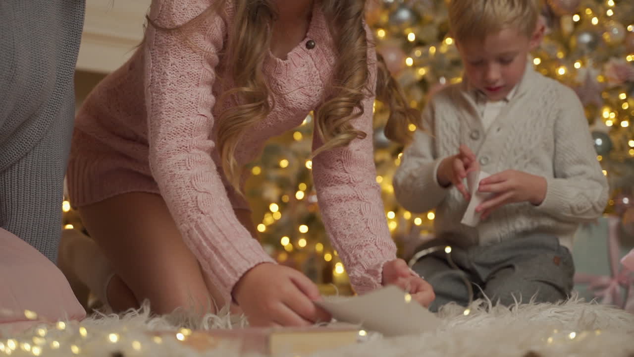 niña y niño escriben una carta en el suelo junto a los regalos y el árbol de navidad