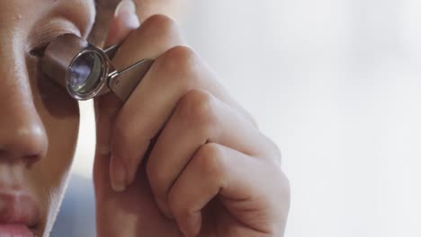 Biracial-female-worker-inspecting-jewellery-with-magnifying-glass-in-studio-in-slow-motion