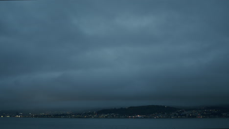 heavy dark clouds over seaside town and water, dark evening with distant lights, handheld
