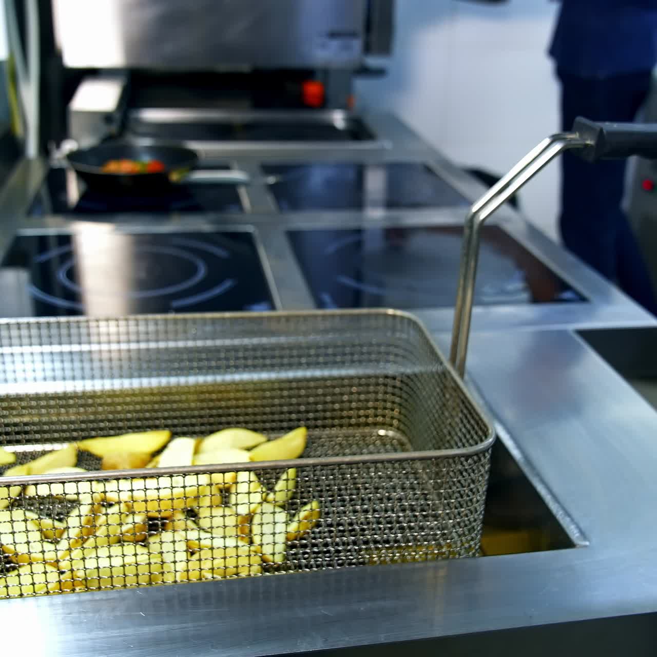 Färdigfriterad potatis i fritös. Tillagade pommes frites i det moderna restaurangköket. Läcker krispig potatis. Snabbmat