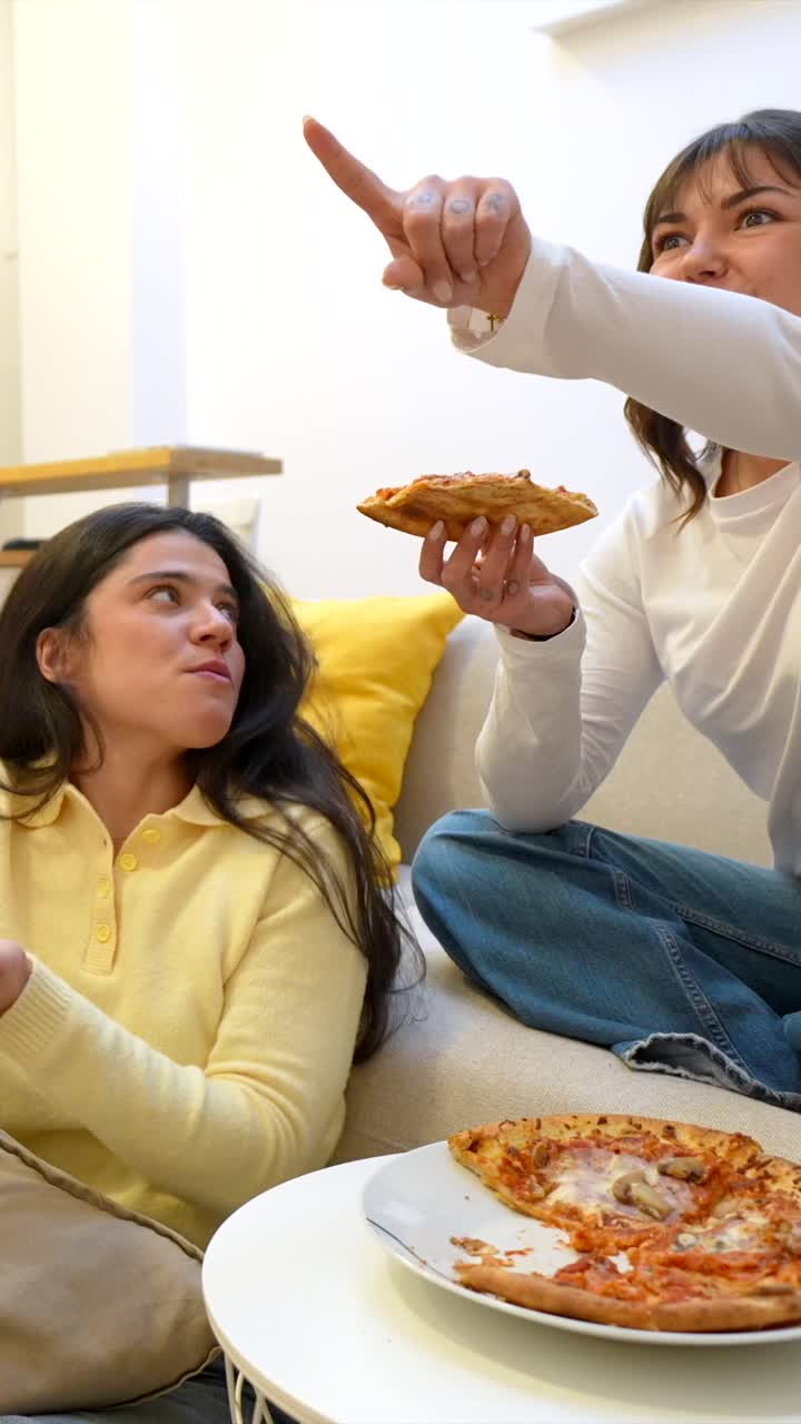 Due giovani donne mangiano la pizza e parlano su un divano a casa
