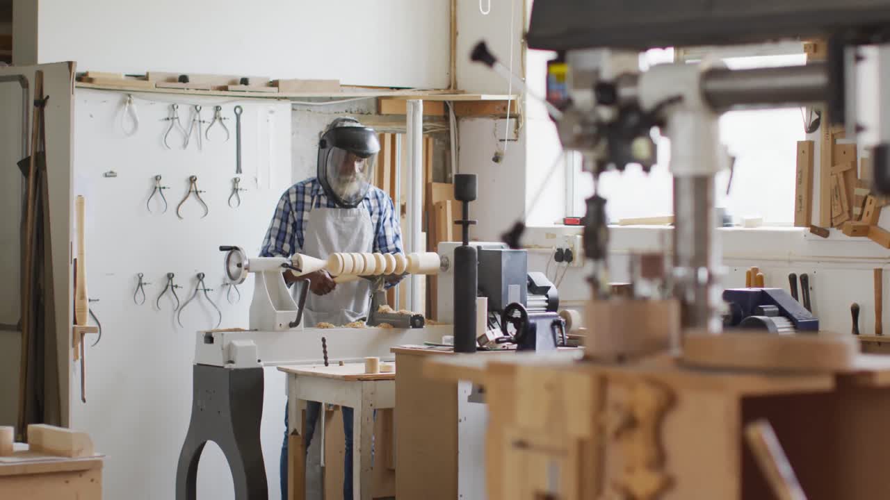 carpintero afroamericano de sexo masculino con casco protector girando madera en un torno en una carpintería