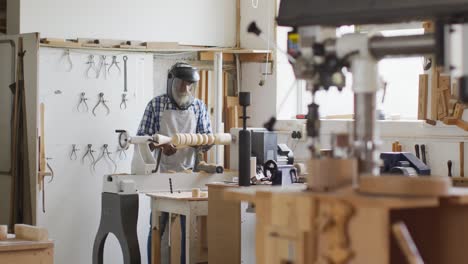 African-american-male-carpenter-wearing-protective-helmet-turning-wood-on-a-lathe-at-carpentry-shop