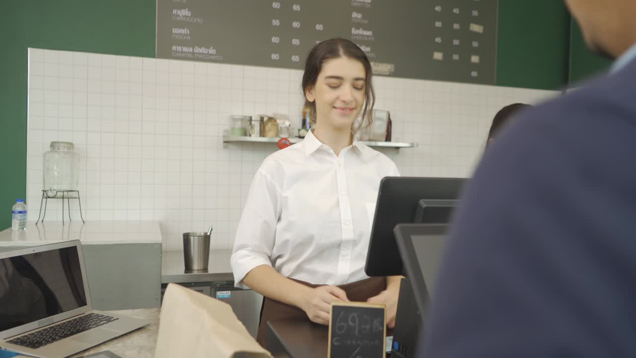 joven barista de oriente medio personas en delantal recogiendo un pago de pedido escaneando el código qr en la pantalla del teléfono, hablando con el cliente en el mostrador, cafetería de cafetería cajero. estilo de vida de la gente. servicio