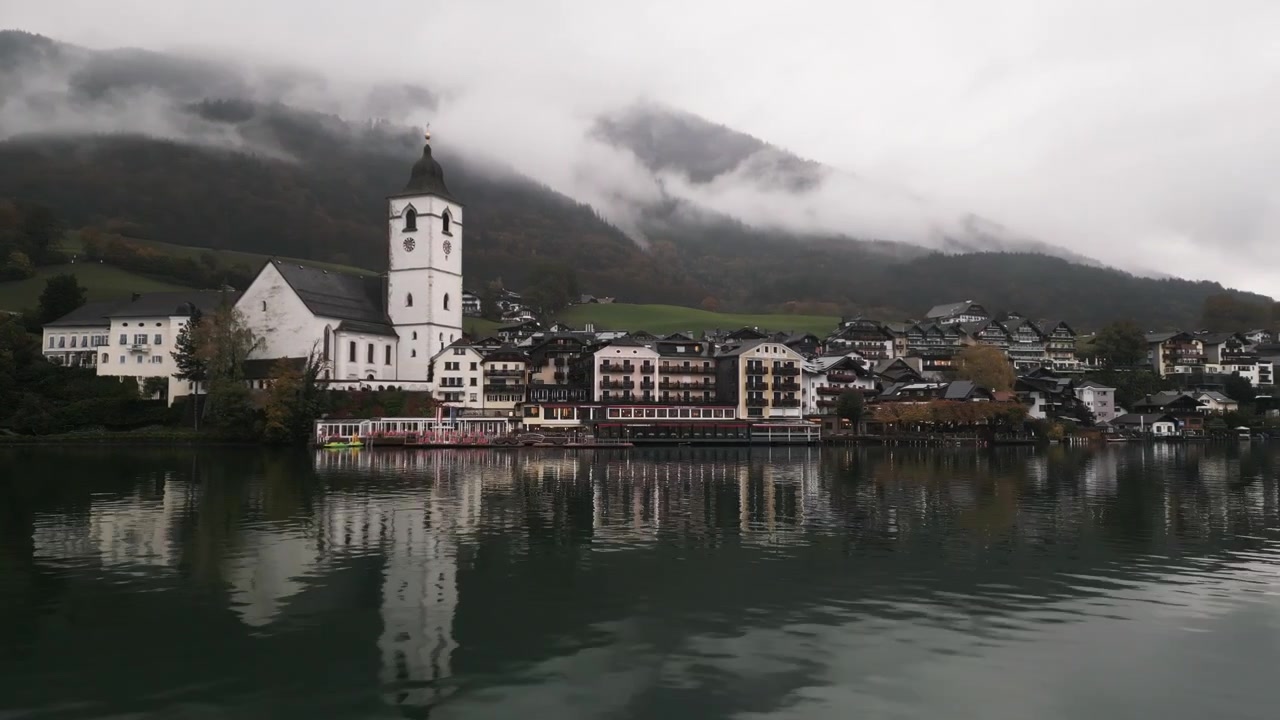 Ripresa aerea ravvicinata in movimento con drone di Wolfgang am Wolfgangsee in una giornata nuvolosa, molto vicino al lago e alle montagne con nuvole su di esse