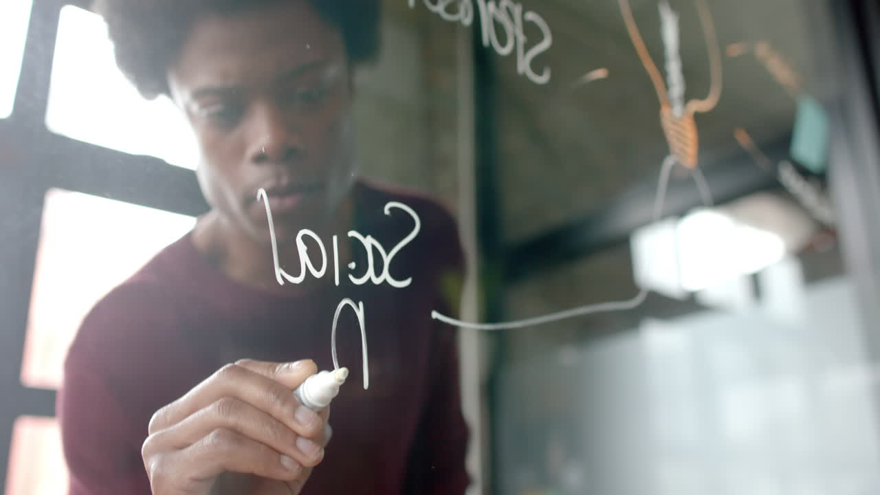 African american casual businessman writing on glass wall at home office, copy space, slow motion