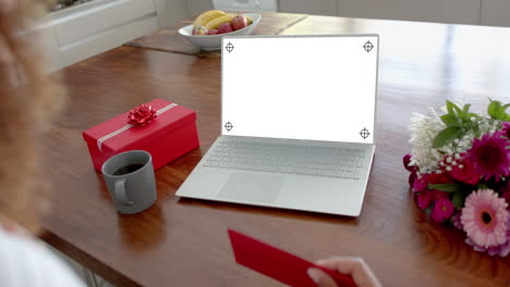 caucasian woman holding red envelope and using laptop with copy space on blank screen