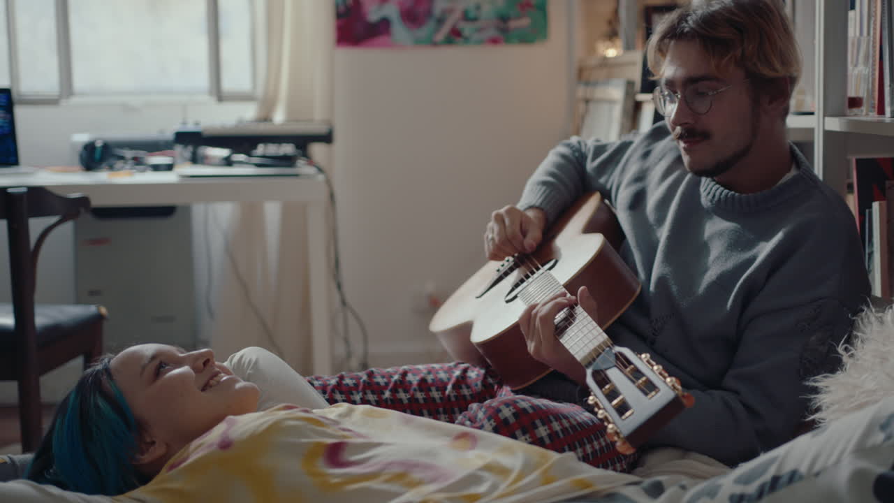 Man Having Wine, Playing Guitar when Resting on Bed with Girlfriend