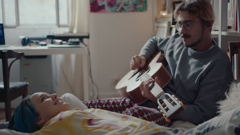 man having wine, playing guitar when resting on bed with girlfriend
