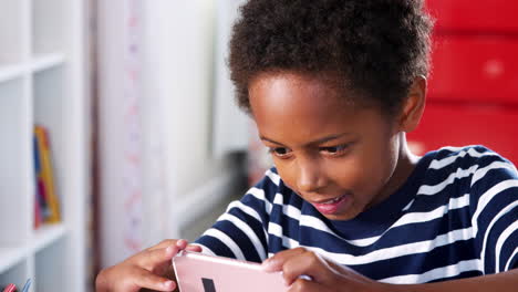 young boy sitting at desk in bedroom playing game on mobile phone