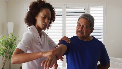 Fisioterapeuta-Femenina-De-Raza-Mixta-Ayudando-A-Un-Hombre-Mayor-Estirando-Su-Brazo