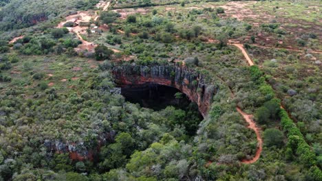 Drone-Aéreo-Inclinándose-Hacia-Abajo-Y-Dolly-En-Una-Toma-Amplia-De-La-Entrada-De-La-Cueva-Lapa-Doce-Con-Una-Selva-Tropical-Autónoma-Debajo-En-El-Parque-Nacional-Chapada-Diamantina-En-Bahia,-Noreste-De-Brasil