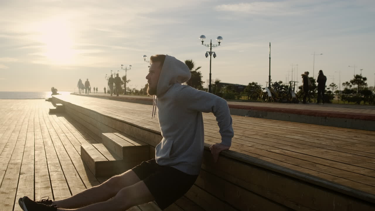 해가 뜨고 해가 지는 바가에 있는 나무 플랫폼에서 푸시업을 하는 남자