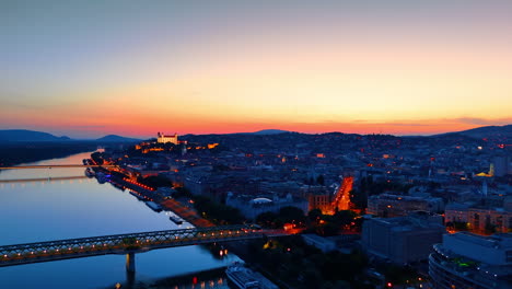 old city is switching on lights at dusk time. drone footage over the danube river near the old bridge in bratislava, slovakia