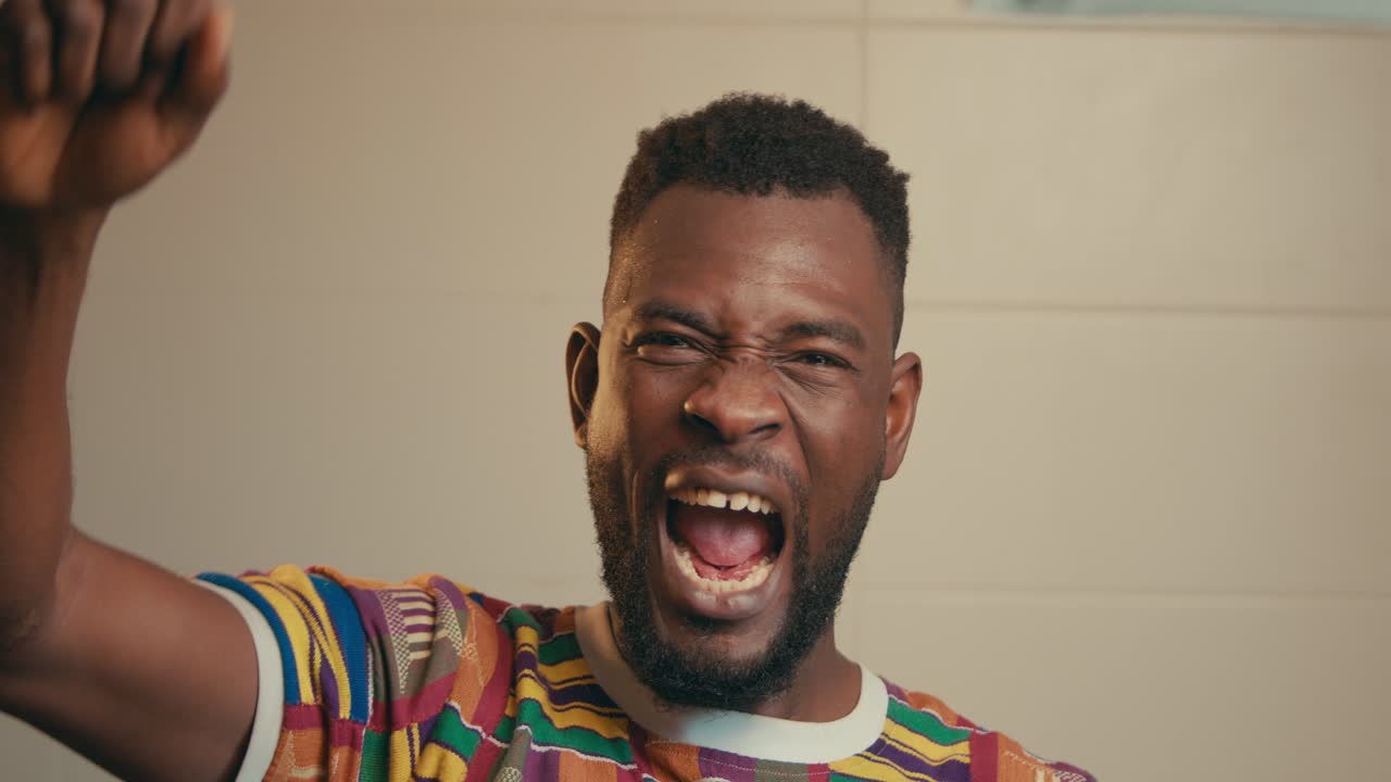 Primo piano di un uomo afroamericano che indossa una camicia in tessuto Kente e festeggia con entusiasmo al rallentatore