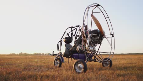 the motor paraglider stands in the field at sunset with a wooden propeller, and the pilot lays out the parachute and aligns the slings