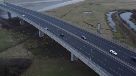 Mersey-gateway-busy-toll-bridge-highway-traffic-driving-across-river-estuary-aerial-view-tilt-up-pan-left