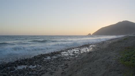 Stationary-shot-of-sunset-over-the-Pacific-Ocean-as-waves-crash-onto-an-empty-beach-located-at-Mondo's-Beach-in-Southern-California-United-States