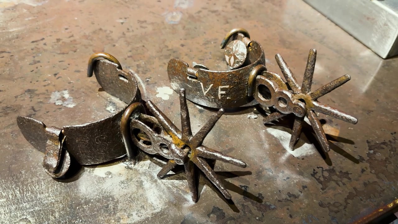 Antiguas espuelas de vaquero de metal descansan sobre un banco de trabajo desgastado, mostrando detalles rústicos y desgaste.