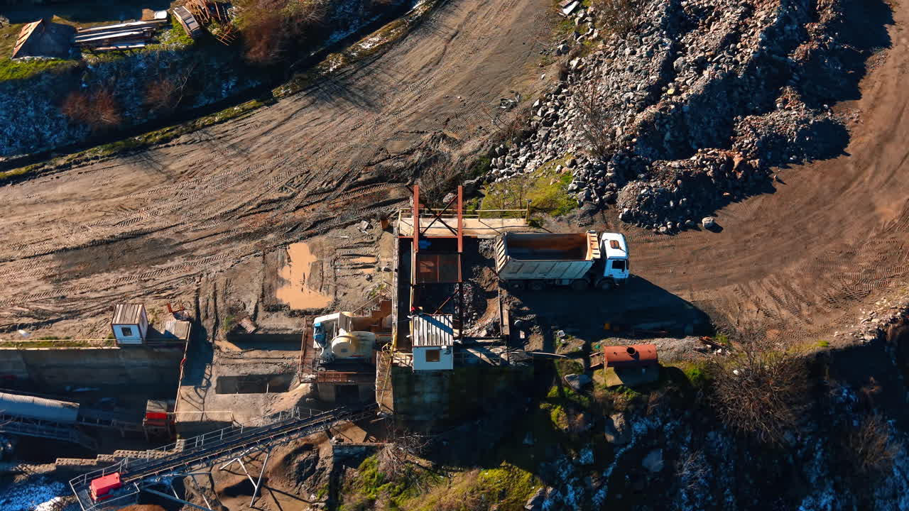 Dumper truck at stone crushing station in quarry. High angle view of a white truck positioned at a crushing unit for granite extraction and processing