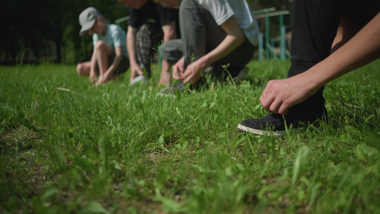 Close-up view of several people lined up on a grassy field, each kneeling down tying their shoelaces