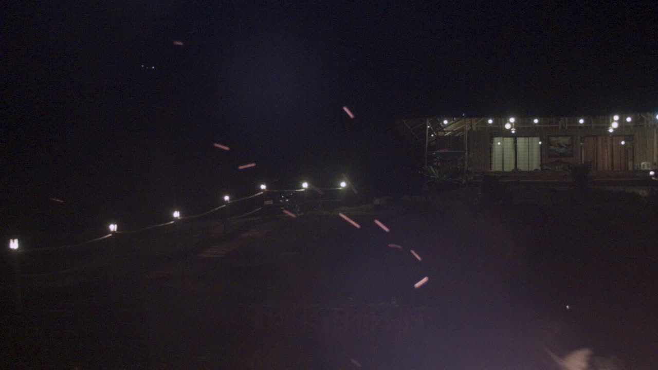Night view of a rustic house with lights and a fire in the foreground
