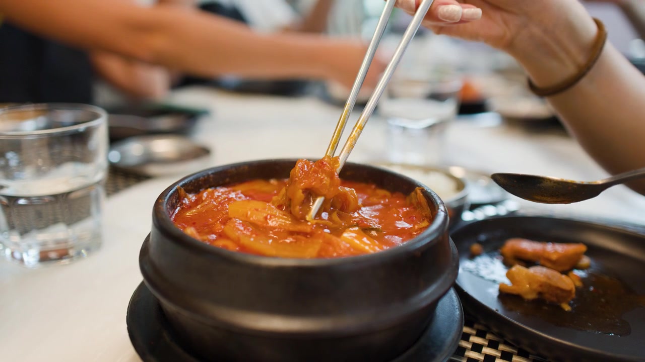 Une personne utilise une cuillère en métal pour manger du kimchi jjigae chaud dans une marmite en pierre