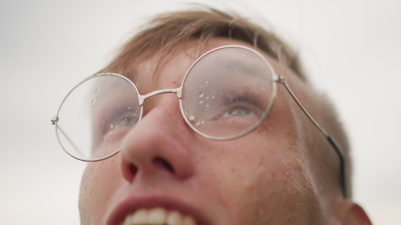 Joyful rainy day, Smile captures moment in light drizzle, Hazy horizon and delighted expression under gentle rain, Candid shot of cheerful youth with rainspeckled glasses and dreamy gaze