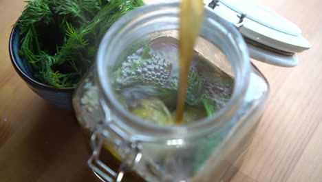 pouring hot vinegar inside a jar filled with cucumber