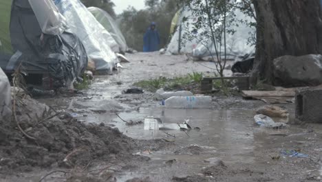 bleak low angle shot moria refugee camp tents in muddy inhumane conditions, rack focus child blue poncho