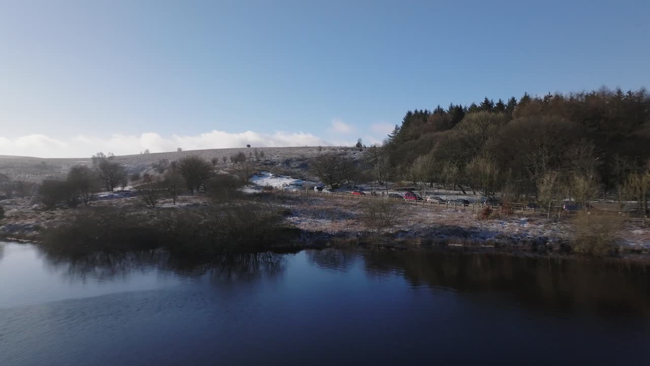 un vuelo de drones sobre un embalse en un camino de invierno congelado y nevado con dos personas caminando hacia un bosque