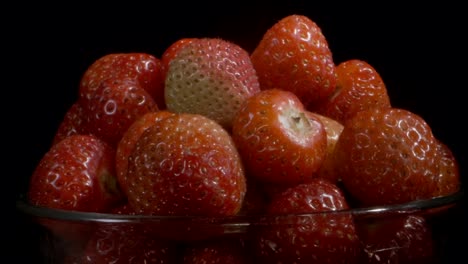 rotar las fresas rojas en vasos de vidrio sobre un fondo negro. rotación de la cámara 360 grados, primer plano.