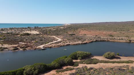 Luftaufnahme,-Die-Einen-Mann-Zeigt,-Der-Stand-Up-Paddle-Auf-Dem-Fluss-In-Exmouth-Mit-Ozean-Im-Hintergrund,-Australien,-übt---Rückwärtsflug